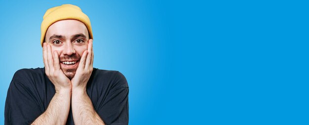 A stunned guy in a yellow cap studio shot on a blue background is depicted with a look of amazement