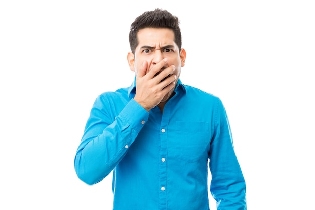 Stunned man covering his mouth in shock over white background