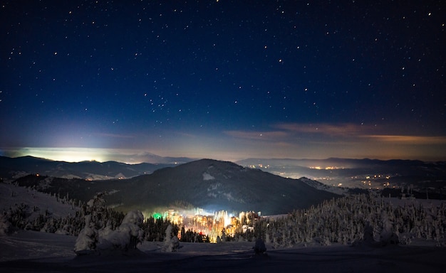 Stunning beautiful views of the ski resort in winter with slopes and firs on a cloudless starry night. Vacation concept in winter and weekend in the countryside. Copyspace