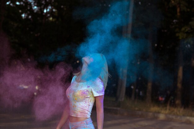 Stunning blonde woman with hair in motion playing with Holi powder exploding around her