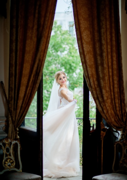 Splendida sposa in un abito da sposa posa sul balcone in una stanza d'albergo di lusso