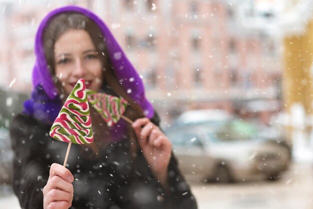 雪片のある通りでカラフルなロリポップを楽しんでいる見事なブルネットの女性。テキスト用のスペース