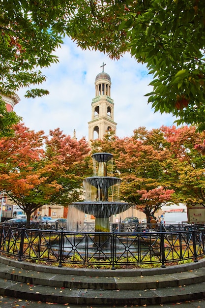 Stunning fountain surrounded by fall leaves in city with Christian Church steeple behind in New York