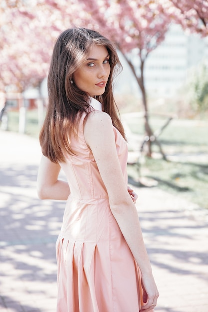 Stunning girl in pink dress standing among sakura trees