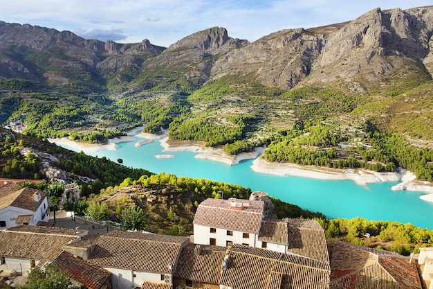 穏やかな青い水が小さな町のある山々の間に隠れているスペインの見事な湖