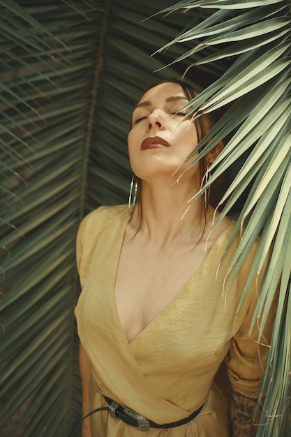 Потрясающая женщина позирует на фоне пальмовых листьев