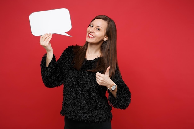 Stunning young woman showing thumb up, holding empty blank Say cloud, speech bubble for promotional content isolated on red background. People sincere emotions, lifestyle concept. Mock up copy space.