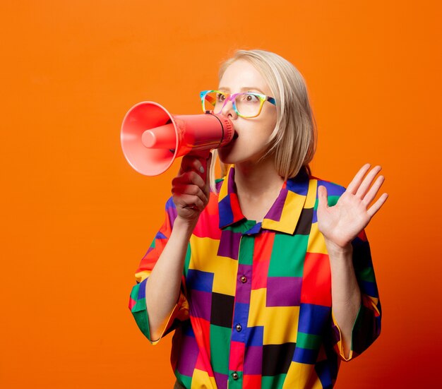 Style blonde in 90s clothes and rainbow glasses with megaphone on orange