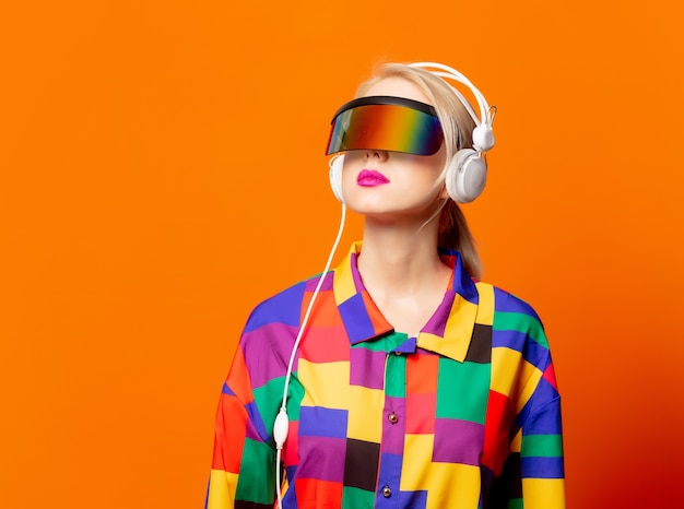 Style blonde in 90s clothes with VR glasses and headphones on orange