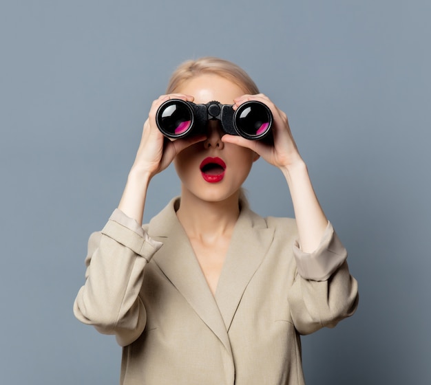 Style blonde in jacket with binoculars on gray space