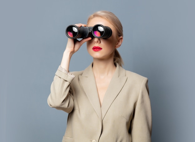 Style blonde in jacket with binoculars on gray space