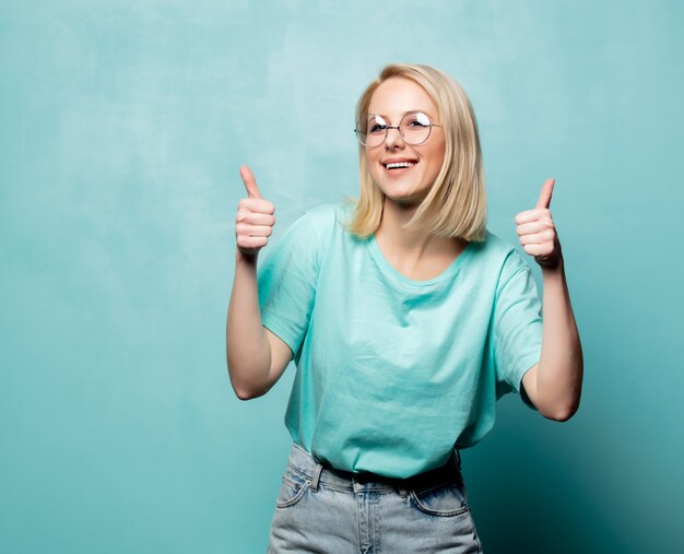 Style blonde woman in glasses show OK gesture on blue wall