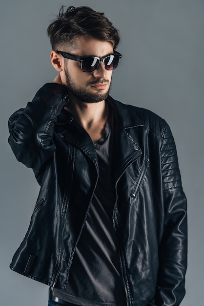 Style and fashion. Confident young man in sunglasses looking away while standing against grey background