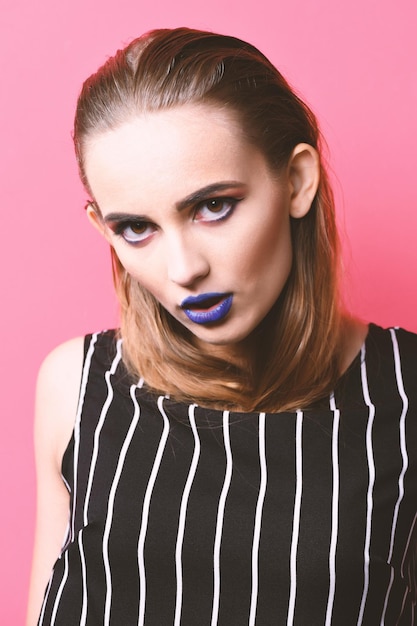 Style and fashion makeup concept. Sexy woman with hair hidden under clothes and blue lips. Girl with seductive face on pink background. Pretty girl in striped black and white blouse