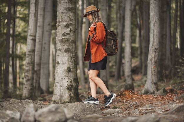 Style girl in hat with backpack in a summer time Mixed coniferous forest