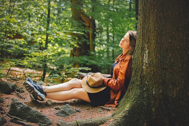 Style girl with backpack sitting in a stone in a summer time mixed coniferous forest