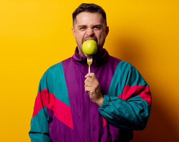 Style man in 90s tracksuit with apple on fork on yellow wall