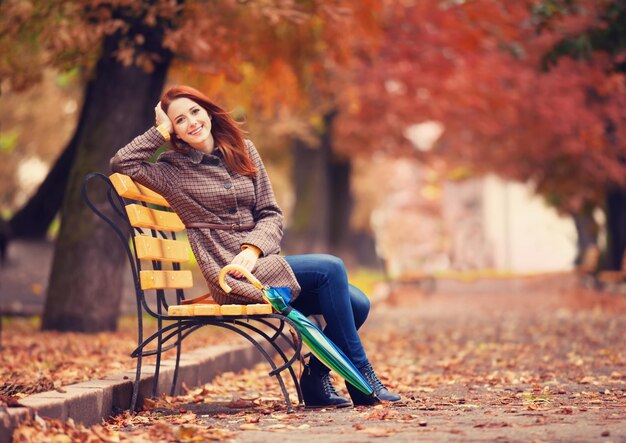 Style redhead girl sitting at bench in autumn park.