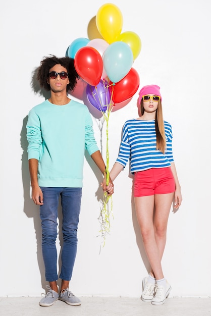 Style with the colorful attitude. Funky young couple holding balloons while standing against white background