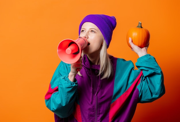 Photo style woman in 90s tracksuit with pumpkin and megaphone on orange