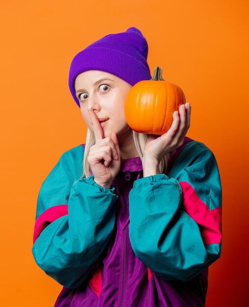 Style woman in 90s tracksuit with pumpkin on orange