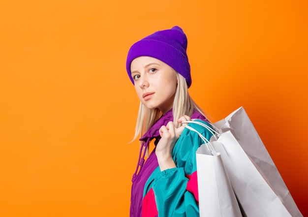 Style woman in 90s tracksuit with shopping bags on orange