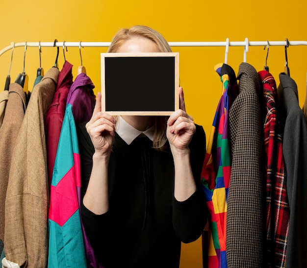 Photo style woman in black formal dress hold board next to clothes on rail hanger