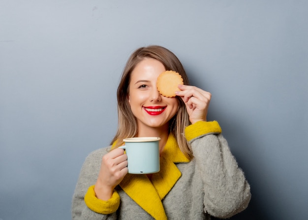 Style woman in coat with cup of coffee and cookie