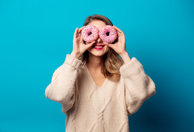 Style woman in sweater with donut on blue wall