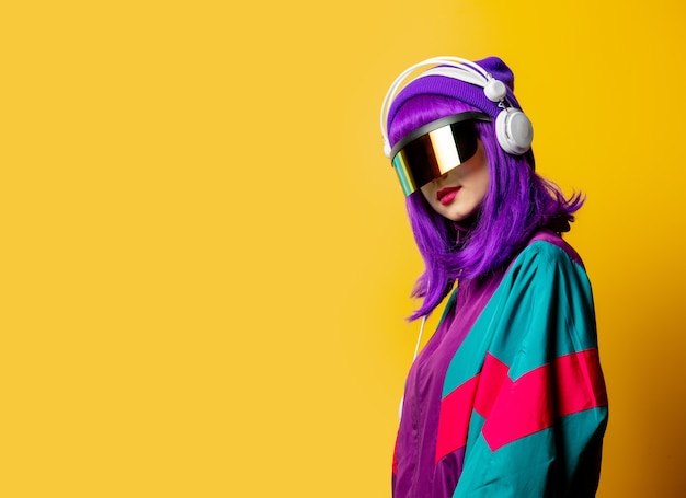 Style woman in VR glasses and 80s tracksuit with headphones on yellow wall