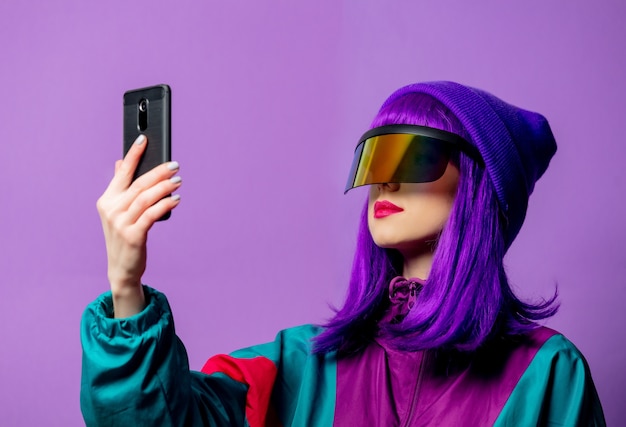 Style woman in VR glasses and 80s tracksuit with mobile phone on violet wall