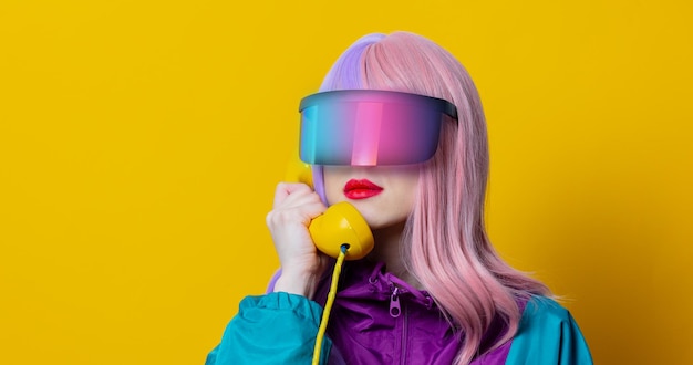 Style woman in vr glasses and 90s sport suit with dial phone on yellow background