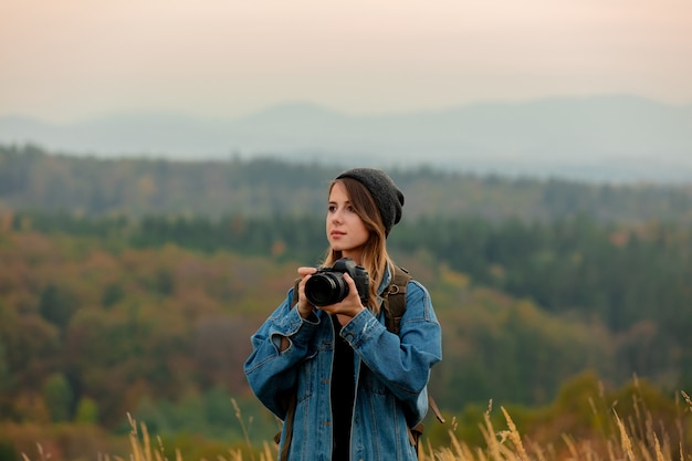 Фото Стиль женщина с фотоаппаратом и рюкзаком в сельской местности с горами