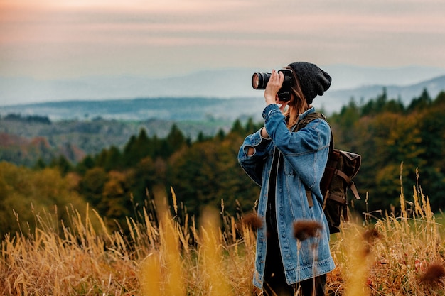 Style woman with photo camera and backpack at countryside with mountains