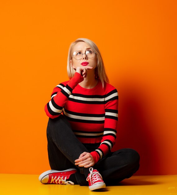 Styled hipster woman sitting on a floor near orange wall