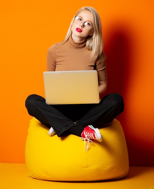Стилизованная хипстерская женщина с ноутбуком сидит в кресле с желтой фасолью на оранжевой стене