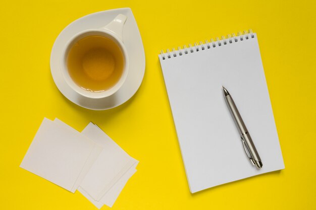 Введенный в моду желтый стол стола офиса фотографии с пустой тетрадью, компьютером, поставками и чашкой тройника.