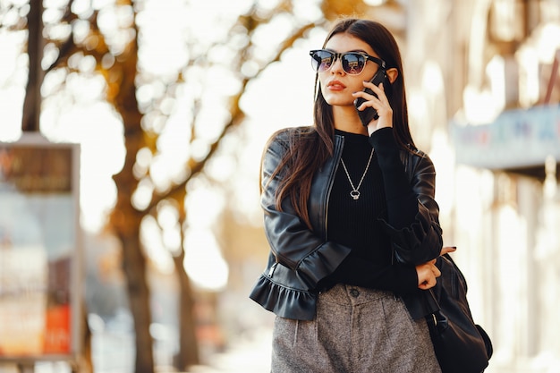 La donna styligh usa il suo cellulare mentre cammina per la città in una giornata soleggiata e calda