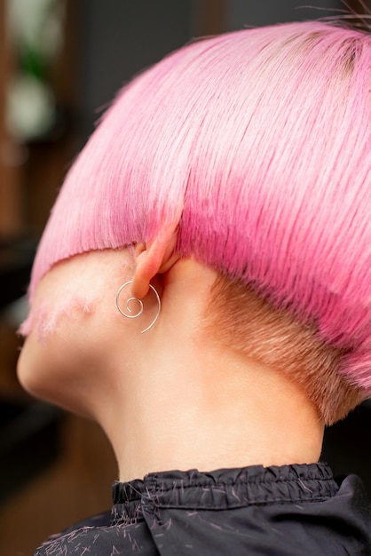 Styling and cutting dyed pink hair of young model back view in a hairdressing salon. Pink short hairstyle.