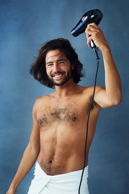 Styling his crowning glory Studio portrait of a handsome young man blowdrying his hair against a blue background