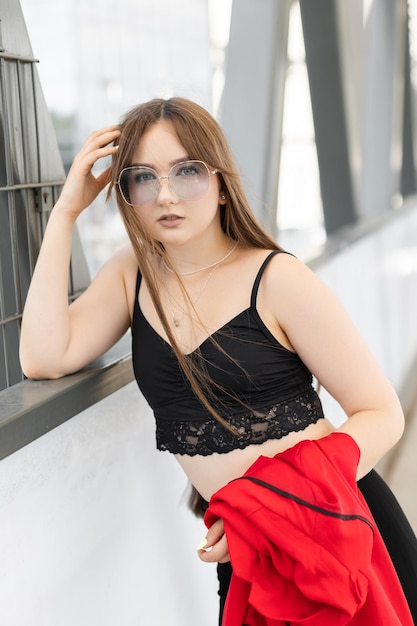 Stylish adorable pretty woman with long hair wearing black stylish suit and sunglasses standing and having fun in the street