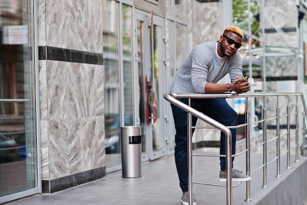 Stylish african american boy on gray sweater and black sunglasses posed at street Fashionable black guy