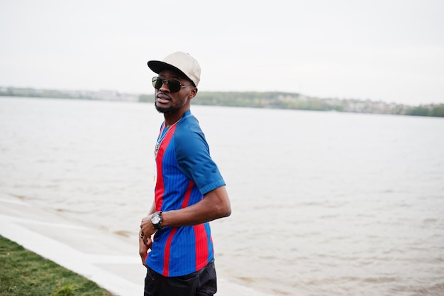 Stylish african american boy wear at cap football tshirt and sunglasses Black sports man portrait