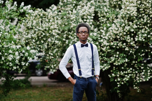 Stylish african american business man at pants with suspender\
and shirt with bow tie hat and glasses posed outdoor