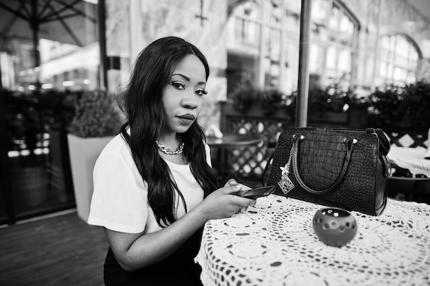 Stylish african american business woman sitting at outdoor cafe with mobile phone