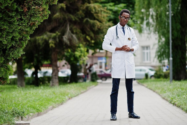 Elegante medico afroamericano con stetoscopio e camice da laboratorio con occhiali in posa all'aperto