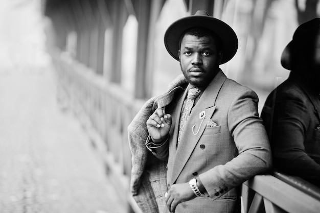 Stylish African American man model in gray coat jacket tie and red hat posed at foggy weather street Black and white photo