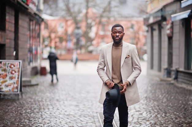 Stylish african american man wear beige jacket and black hat pose at street.