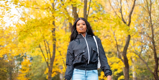 Elegante donna afroamericana in abiti casual alla moda all'aperto su uno sfondo di fogliame autunnale giallo brillante