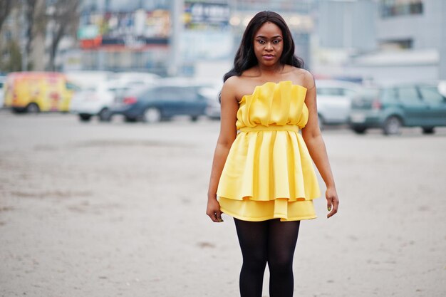노란 드레스를 입은 세련된 아프리카계 미국인 여성이 야외 주차장을 포즈를 취했습니다.